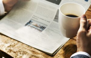 A person drinks coffee while reading an investment newsletter at a table