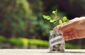 A jar full of coins with the word emergency on it representing an emergency fund.